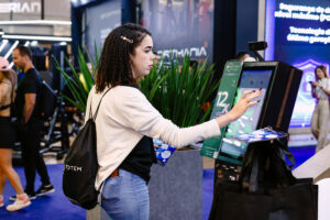 Stand da Pacto no Arnold Classic 2025 com visitantes conhecendo o Pacto Flow em totem de autoatendimento
