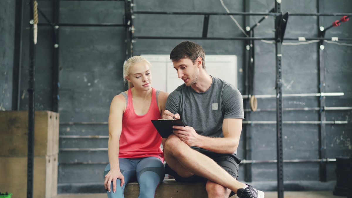 Personal trainer revisando progresso de aluno em tablet em academia, contexto de venda de pacotes e aumento de ticket médio